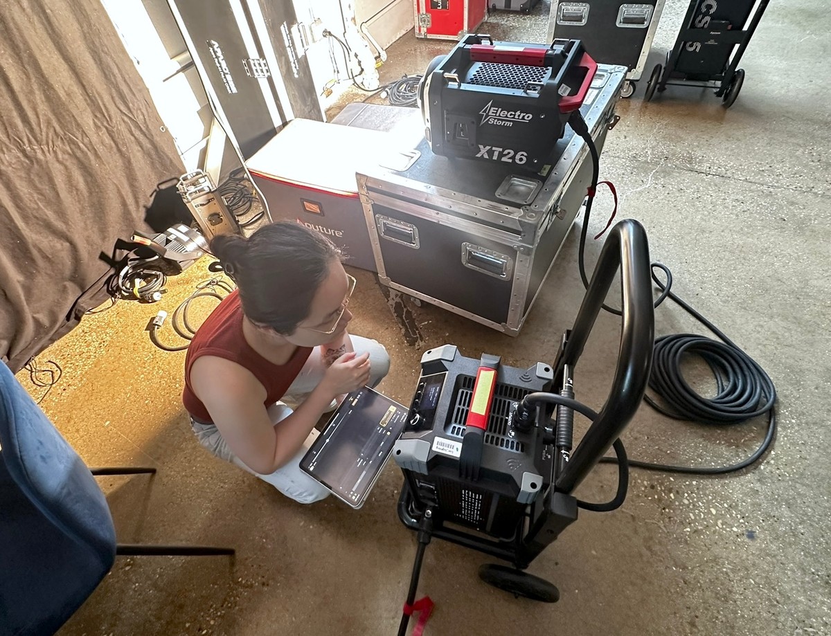 Chi crouched on a stage floor with an iPad running Slyyd, verifying a profile against a professional LED fixture on set