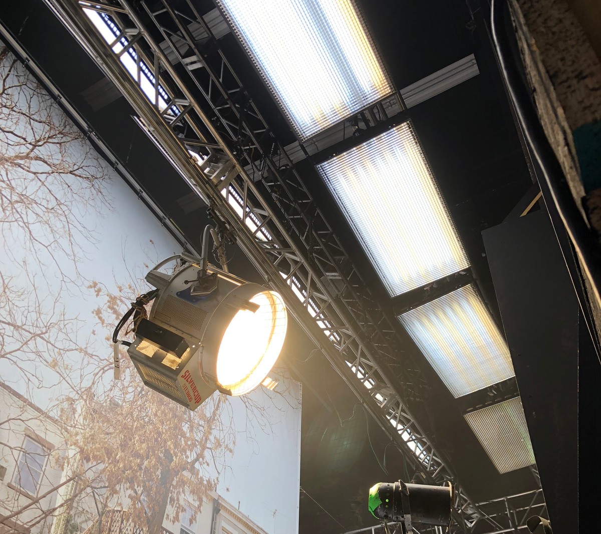 Stage interior with tungsten globe heads gelled with color-temperature blue, aimed through a window backdrop as a daylight source