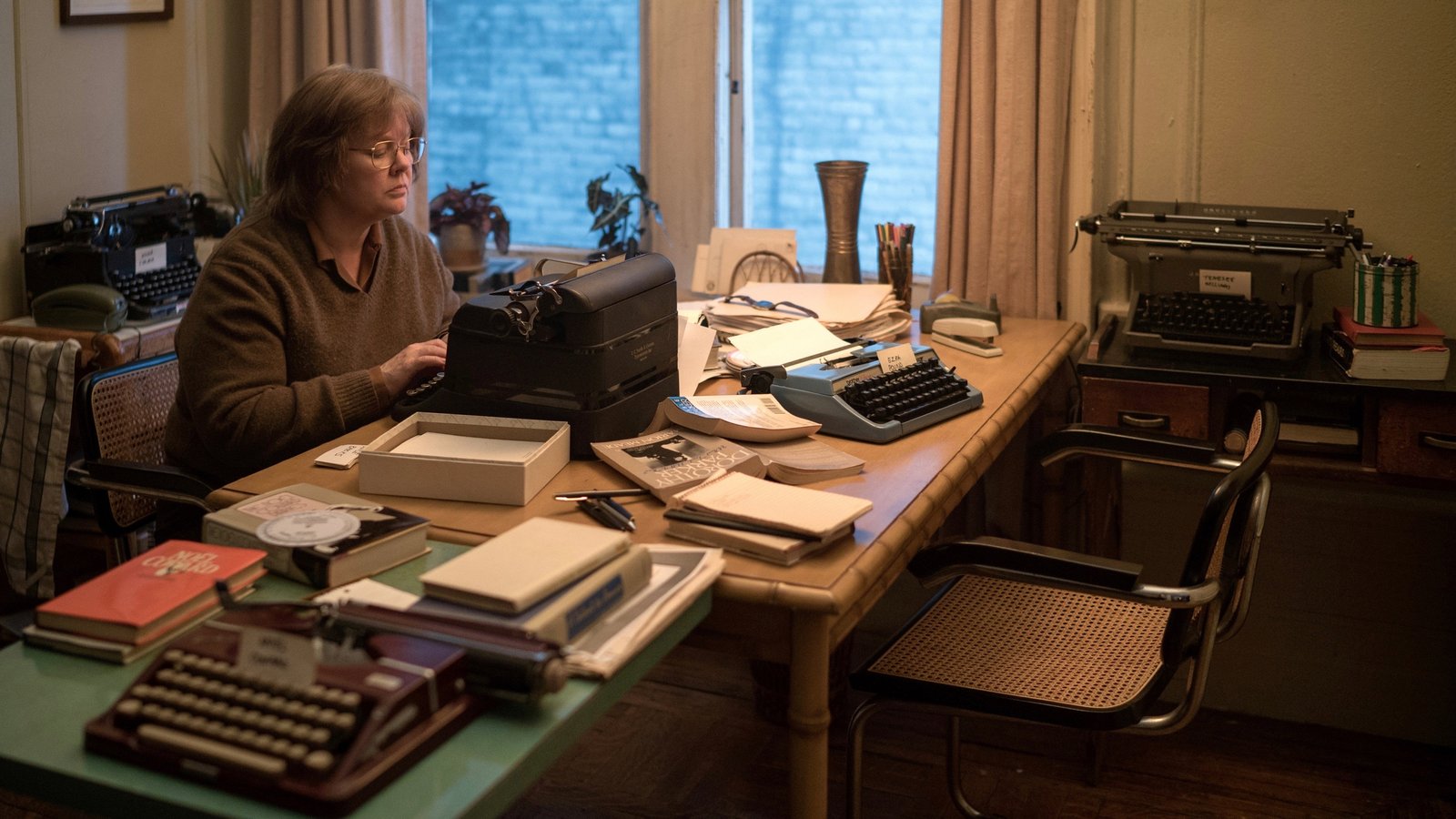 Lee Israel at her writing desk in daylight, typewriter collection in foreground