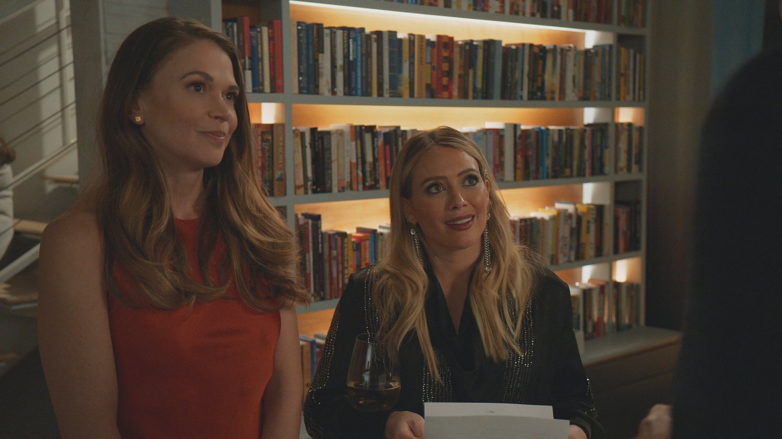Liza Miller and Kelsey Peters at warm-lit bookshelves with wine — Younger, Season Seven